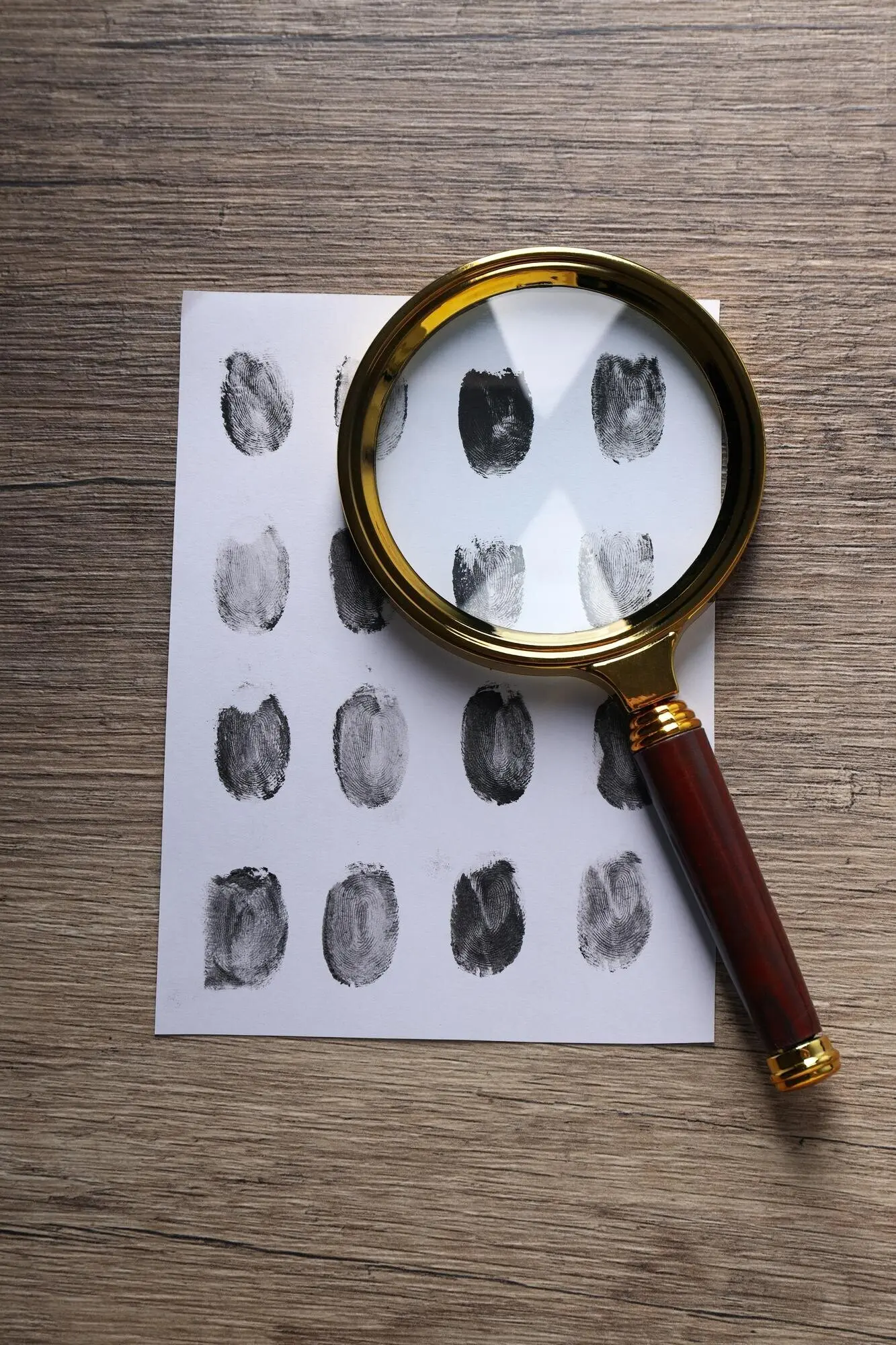 A magnifying glass and an envelope with fingerprints on a wooden background.